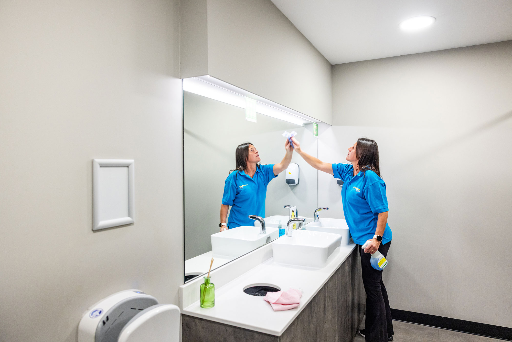 Women cleaner cleaning bathroom mirror